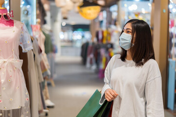 woman holding shopping bag and looking to clothes at mall and her wearing medical mask for prevention from coronavirus (Covid-19) pandemic. new normal concepts