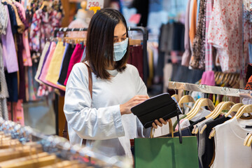 woman open purse to payment for clothes at shopping store and her wearing medical mask for prevention from coronavirus (Covid-19) pandemic. new normal concepts