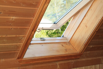 Open dormer window in wooden house in the attic. Room has sloping ceiling made of natural...