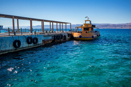 Aqaba, Jordan - February 2, 2020: Big tourist boat with glass bottom, painted in orange waits at the port for tourists to take a trip at Red Sea. Cloudless clear sky winter day. Horizontal frame