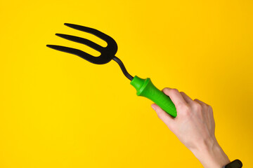 HAnd holding mini garden fork on a yellow studio background. Top view