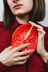 Faceless portrait of young woman holding red red bloom peace lilly (Spathiphyllum wallisii)