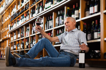 Fine man tasting red wine sitting on floor