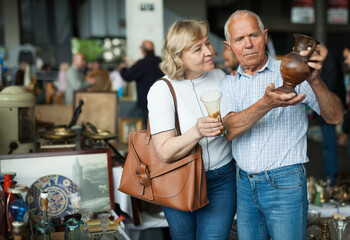 Smiling mature spouses buying retro handicrafts on flea market