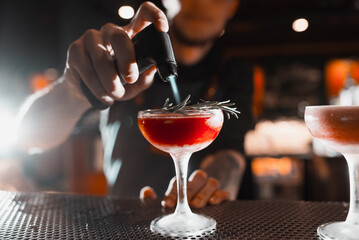 The bartender prepares red alcoholic cocktails at the bar
