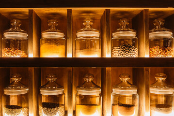 Decorative glass jars with spices on the kitchen shelf. Warm tint
