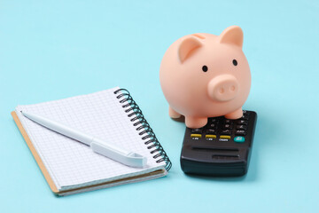 Piggy bank, notebook and calculator on blue background. Minimalistic studio shot.