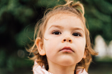 Toddler girl close up portrait. Serious child outdoors in park. Camping concept. 
