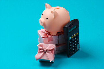 Piggy bank on stack of gift boxes and calculator. Blue  background