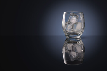 Shaved ice cubes in a low whiskey glass with dark reflections on a dark background.