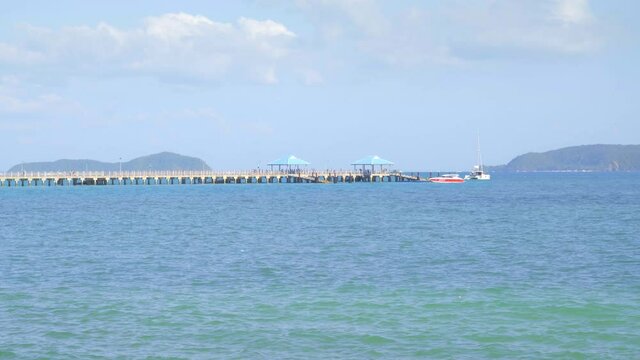 People are walking from pier in bright blue water near tropical beach with islands in foggy background