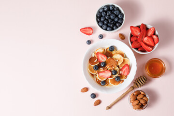 Pancake cereal with berries and honey on pink background