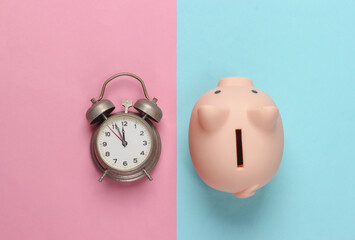 Piggy bank and retro alarm clock on blue pink background. Minimalistic studio shot. Overhead view....