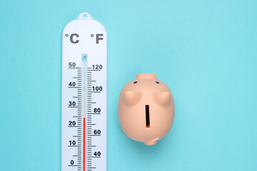 Piggy bank and weather thermometer on blue pastel background. Minimalistic studio shot. Overhead...