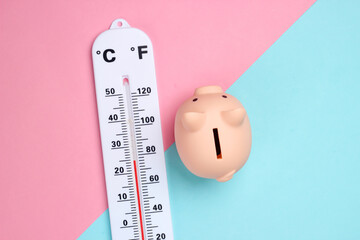Piggy bank and weather thermometer on pink blue pastel background. Minimalistic studio shot....