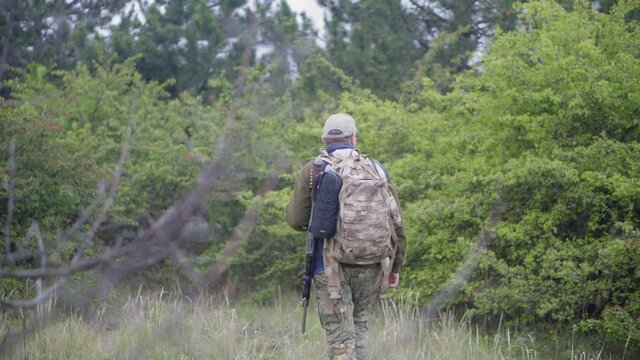 A hunter with a rifle and a backpack goes into the forest