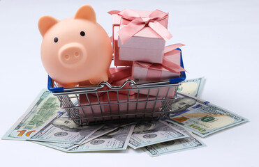 Supermarket basket with piggy bank, gift boxes on hundred dollar bills