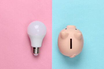 Piggy bank and led light bulb on blue pink pastel background. Energy saving. Minimalistic studio...