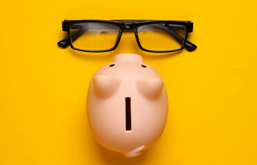Piggy bank and glasses on yellow background. Minimalistic studio shot. Overhead view. Flat lay.