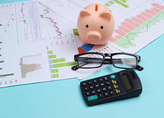 Piggy bank with graphs and charts, calculator, glasses on a blue background. Economic analysis,...