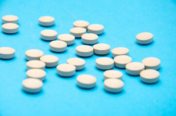 Round white, yellow pills on a blue background top view, side view in macro. Place for text. The tablets lie chaotically on the right, on the left in the middle. Pills in macro