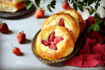 Homemade buns with cottage cheese and strawberries (cheesecakes) in a dish on a gray background, Russian cuisine