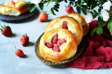 Homemade buns with cottage cheese and strawberries (cheesecakes) in a dish on a gray background, Russian cuisine