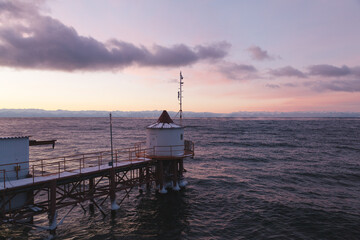 Purple december sunrise landscape of Baikal Lake with dramatic clouds and haze over mountains and waves and water intake tower in the foreground, Listvyanka