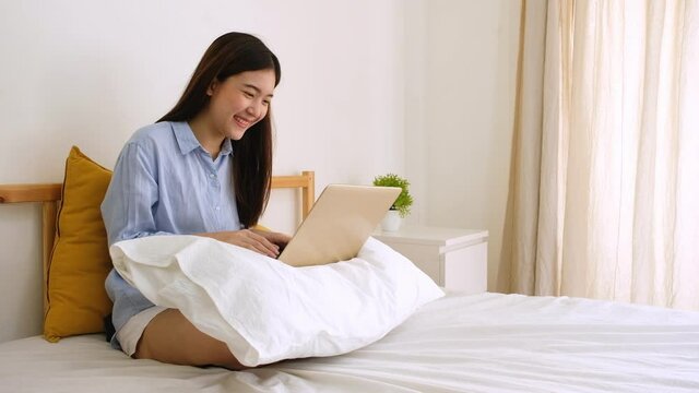 Young asian woman using computer laptop work from home on bed.