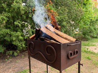 Hot grill during a picnic in the yard. Metallic roaster with coal in the park. The fire burns in a...