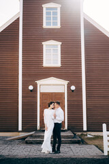 Destination Iceland wedding. Wedding couple in front of a black church. The groom hugs the bride.