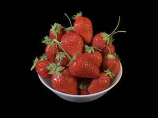 Red, ripe strawberries on a black background. Early berries on a white dish. Sweet berry on a plate.