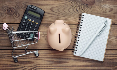 Shopping concept, economy. Shopping list. Piggy bank with supermarket trolley and calculator,...