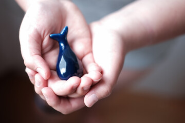 human hands holding blue whale. save whales and protect nature. eco activism concept. ceramic blue...