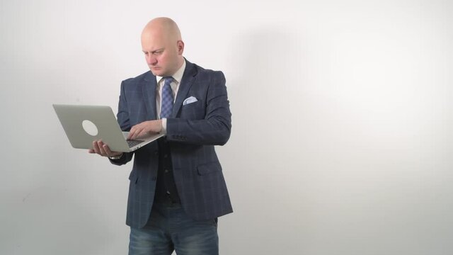 A bald man holds a laptop with a surprised face and asks questions.