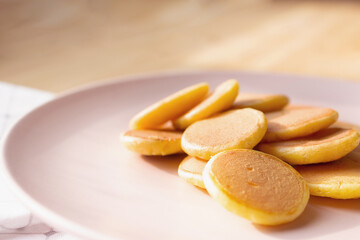 Amazing delicious trendy tiny pancakes cereal on gently pink plate. Wooden table background.