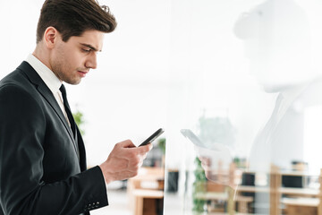 Image of serious businessman wearing black suit using mobile phone