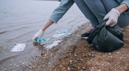 female volunteer removes debris from used medical masks and gloves on the beach and in the water