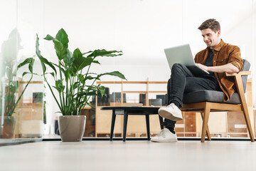 Image of handsome happy caucasian man smiling while working with laptop