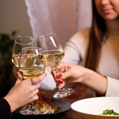female friends - hands clinking white wine glasses, restaurant or bar on background, close up view. evening, celebration and holidays concept