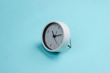 Fototapeta na wymiar White clock on blue background. Minimalistic studio shot.
