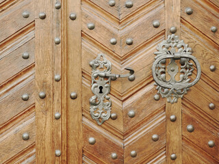 Old wooden door with rivets. Metal handle and door lock.