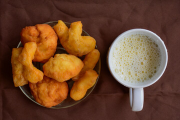 deep-fried doughstick on plate , dish and soymilk in a white glass both on brown background.