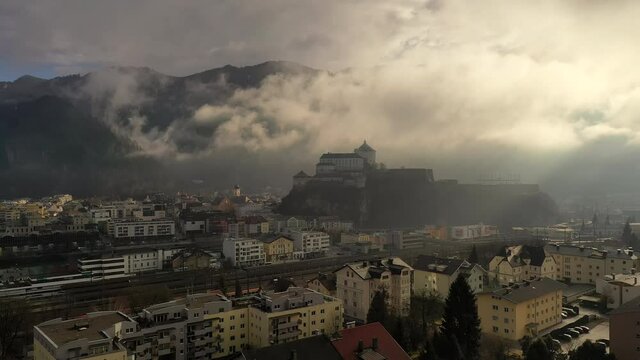 Aerial view of mountain town Kufstein with medieval hilltop fortress, dramatic winter scenery at sunrise, river Inn meandering through the valley - Austrian Alps from above, Tyrol, Austria, Europe