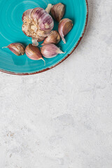 A whole head and cloves of purple garlic on a turquoise plate on a white textured background, top view, copy space