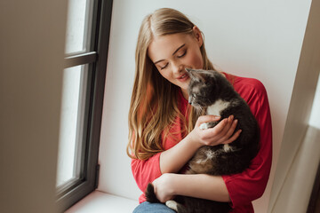 selective focus of young woman looking at cute cat near window