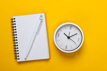 Fototapeta na wymiar White clock and notebook on yellow background. Minimalistic studio shot. Top view