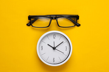 White clock with glasses on yellow background. Top view