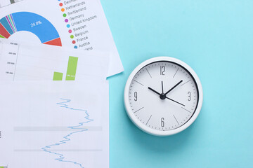 Time to make money, invest. Graphs and charts, clock on a blue background. Business concept. Top view
