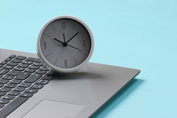 Laptop and alarm clock on blue background. Time running away. The concept of urgent deadlines at work and commitments